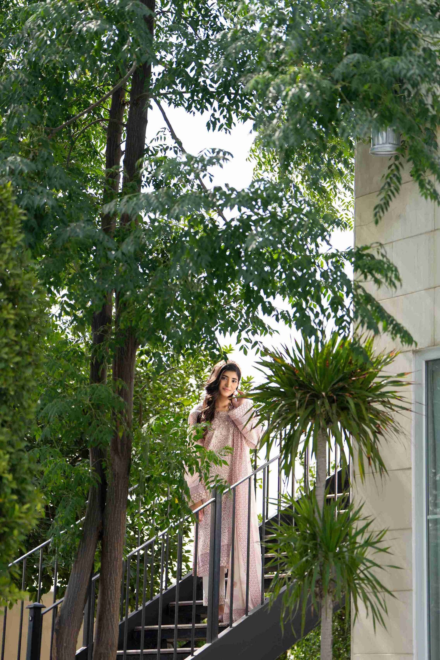 Woman in peachy pink threadwork 3-piece suit with slim trousers and airy dupatta, glowing in subtle summer sophistication