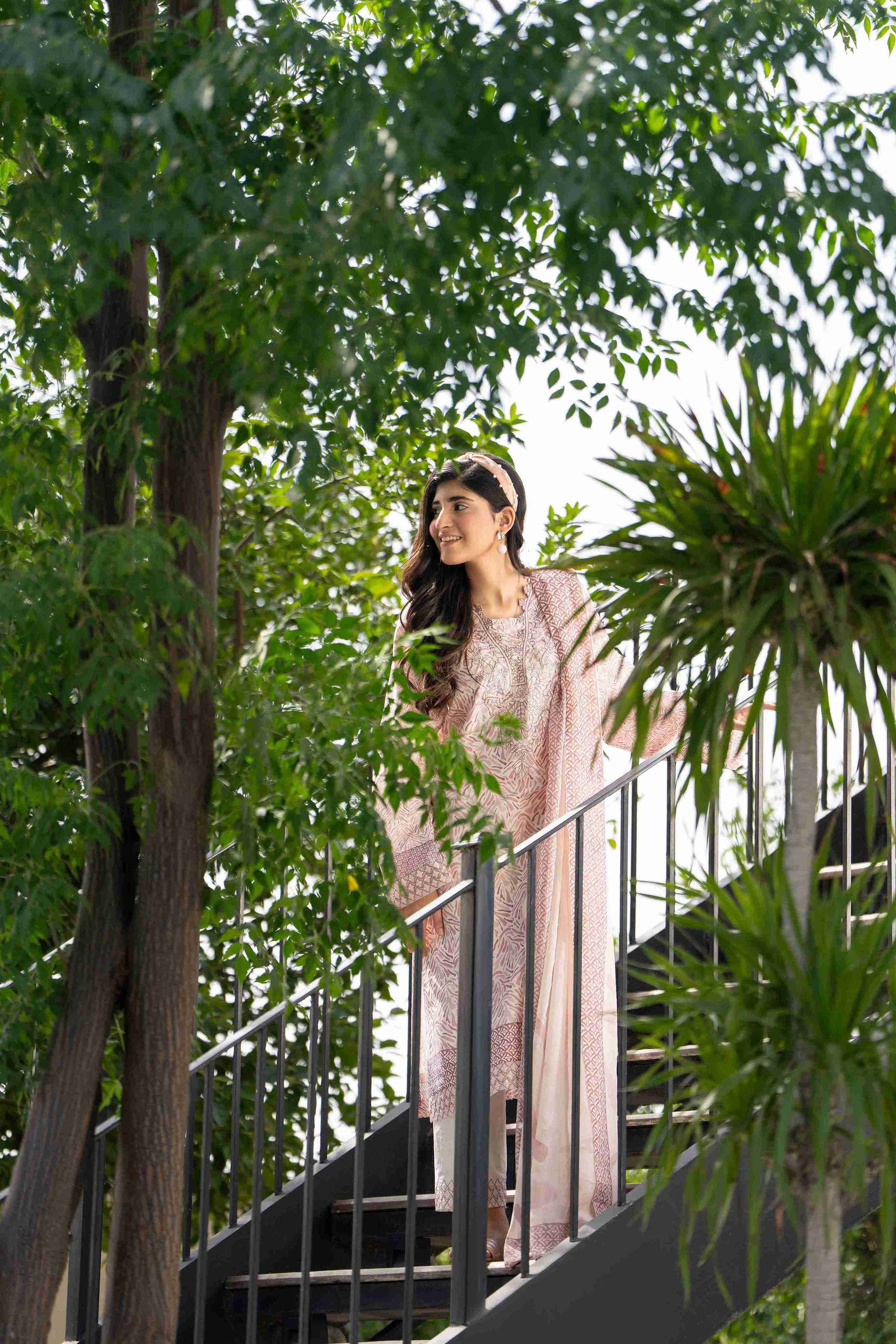 Pakistani luxury womenswear -  pastel pink embroidered dress with dupatta, styled outdoors in a greenery-filled fashion photoshoot