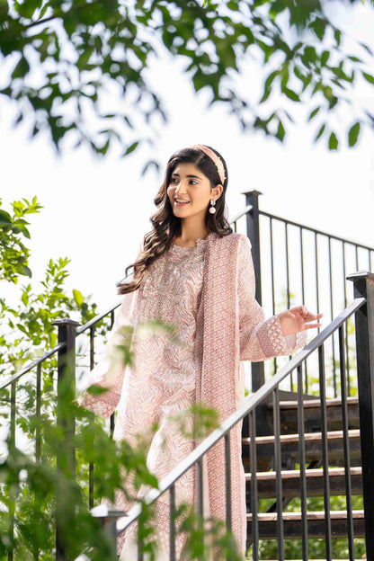 Woman in pastel pink floral lawn 3-piece with ivory trousers and sheer dupatta, walking gracefully in breezy summer style