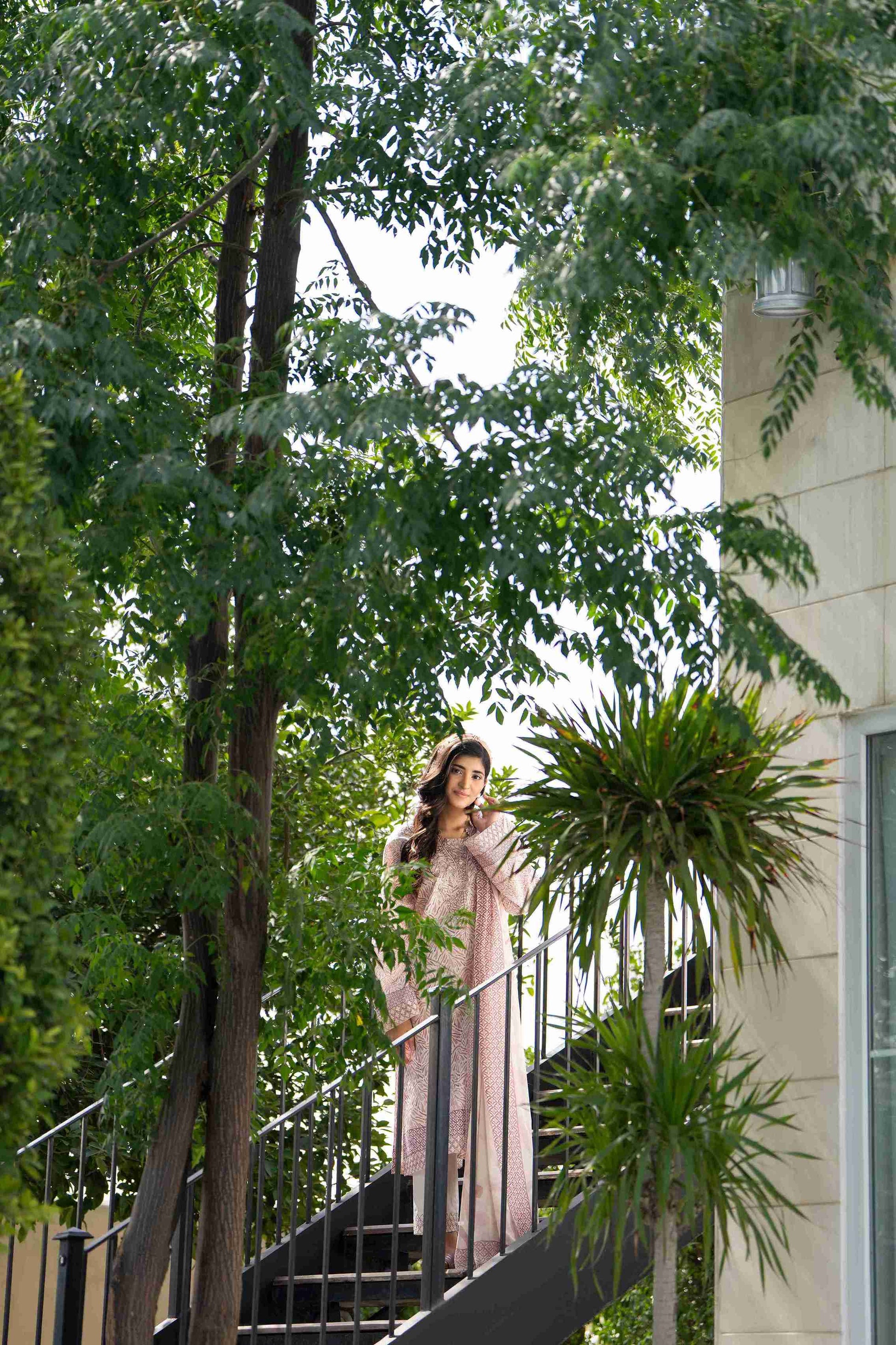 Woman in peachy pink threadwork 3-piece suit with slim trousers and airy dupatta, glowing in subtle summer sophistication